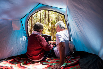 Fototapeta na wymiar Elderly alternative travel lifestyle for old senior people sit down inside a tent with modern device - concept of youthful and no limit age to enjoy the world and life