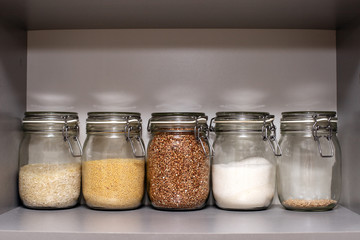 glass jars of buckwheat, wheat, rice, sugar, and the remnants of pearl barley are in an empty kitchen Cabinet