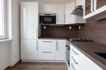 A modern L-shaped wooden kitchen with a dark brown desk and white colours and embedded refrigerator