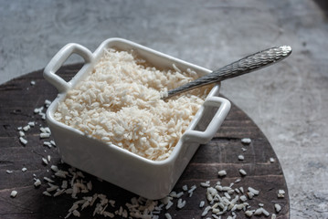 Coconut flakes in a square square bowl with handles on a wooden round board on a concrete tabletop...