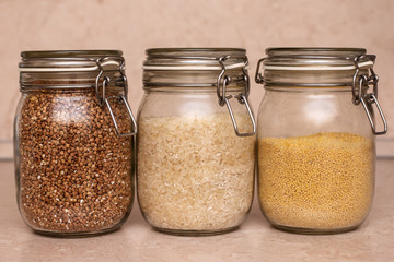 glass jars with buckwheat, wheat groats and rice stand on a wooden table