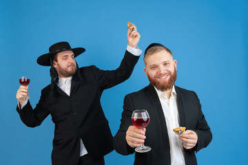 Dancing with wine, having fun. Portrait of a young orthodox jewish men isolated on blue studio...
