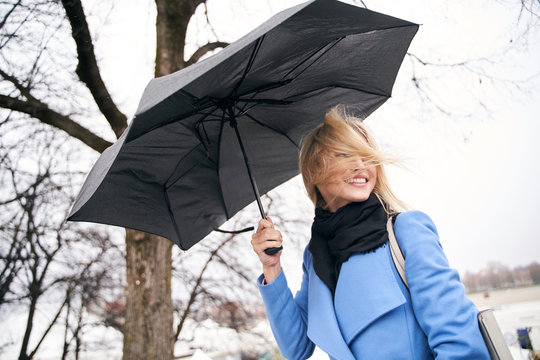 Smiling blond woman holding umbrella in storm