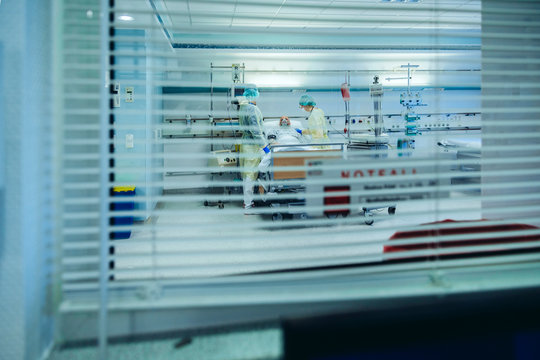 Doctors behind sunblind caring for patient in emergency care unit of a hospital with respiratory equipment