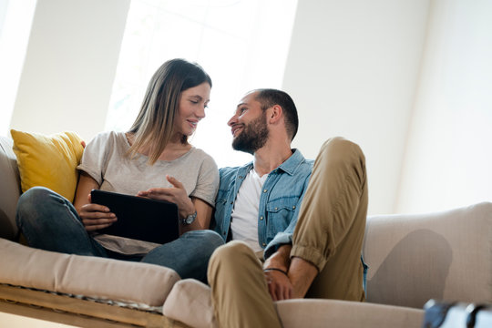 Happy young couple relaxing on couch at home with tablet