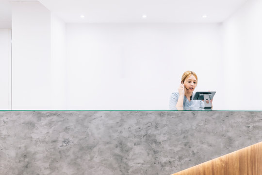 Receptionist at reception desk of a medical practice using headset and digital device