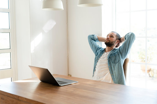 Serious young man with laptop in home office having a break