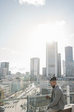 Stylish man using smartphone on observation terrace with skycraper view, Frankfurt, Germany