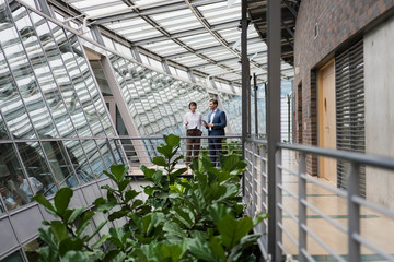 Businessman and woman talking in sustainable office building, using digital tablet