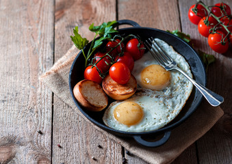 Fried eggs in a pan with cherry tomatoes and bread for breakfast. Breakfast concept. Wood background.
