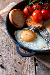 Fried eggs in a pan with cherry tomatoes and bread for breakfast. Breakfast concept. Wood background.