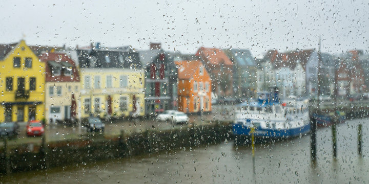 Germany, Schleswig-Holstein, Husum, Waterfront houses seen through window glass covered in raindrops