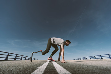 Disabled athlete with leg prosthesis in starting position on a road