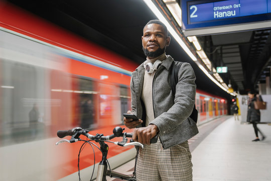 Stylish man with a bicycle, headphones and smartphone in a metro station