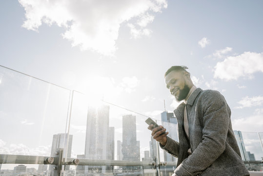 Stylish man using smartphone on observation terrace with skycraper view, Frankfurt, Germany