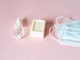 Flat lay personal protective equipment against various viruses - medical masks, bottle sanitizer and piece soap on pink background. Copy space.