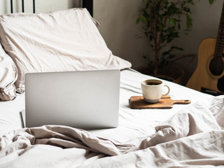 Laptop and coffee on the bed and a guitar next to the bed in the bedroom. Work from home or comfortable pastime online. Stay home, quarantine. Work at home concept.