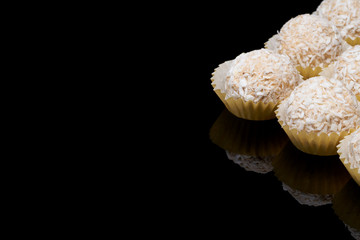White coconut balls, raw and healthy sugar free rafaello candies on black glass background. Covering balls in coconut shred. Vegan, vegetarian sweets