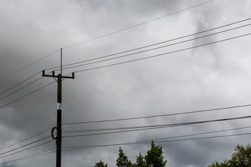 Electricity pole and high voltage power lines on the road with cloud and overcast sky