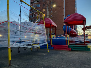 Fototapeta na wymiar Closed children's playground in the city. empty playground during the quarantine coronavirus. kids playground wrapped with red-and-white warning tape. forbidden to visit the communal play area