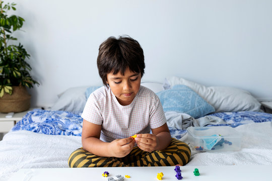 Boy sitting on bed playing with building blocks
