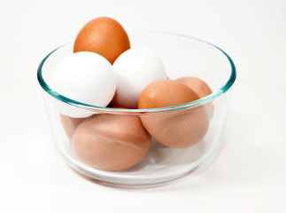 Brown and white eggs in a glass bowl close up against a white background.