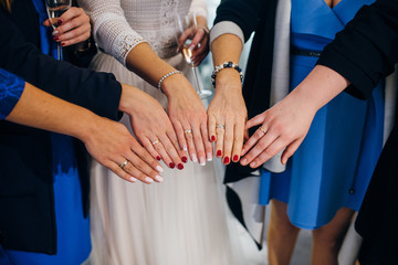 Bride and bridesmaids showing their hands with wedding rings on them, holding glasses with champagne