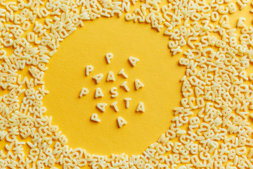 Top view of the macaroni alphabet and the inscription in a circle, on a bright yellow background
