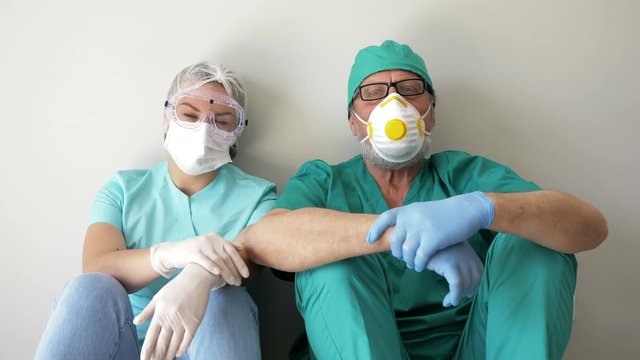 Tired doctor and nurse are resting sitting on the floor in a hospital corridor.