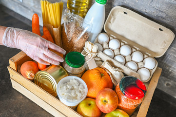 Volunteer hands in medical gloves holding donation box with various products for poor people. Pandemic coronavirus food shortages. Food donations or delivery concept. Free space for text copyspace