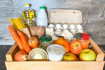 Donation volunteer box with various products for poor or elderly people on wooden background. Pandemic coronavirus food shortages. Food donations or delivery concept. Free space for text copyspace