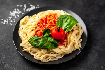 
Italian pasta spaghetti with tomato sauce and herbs on a black plate on a stone background