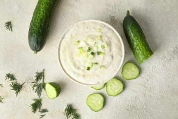 Delicious yogurt sauce with cucumber in bowl on white background