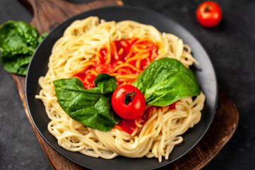 
Italian pasta spaghetti with tomato sauce and herbs on a black plate on a stone background