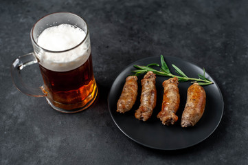 Beer and grilled sausages with spices, tomatoes, rosemary on a stone background with copy space for your text
