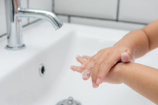 Kid Washing Hands In A White Basin With A Bar Of White Soap.