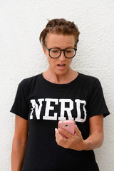 Shocked mature nerd woman wearing big eyeglasses and standing against white background outdoors...
