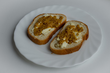 Two pieces of bread with wholegrain mustard and butter on white plate on light white background