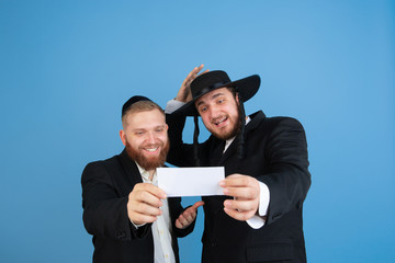 Winning lottery ticket. Portrait of a young orthodox jewish men isolated on blue studio background....