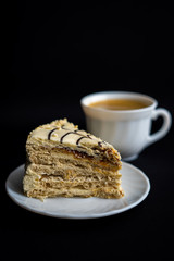 Piece of delicious sweet cake on white plate and a cup of coffee on dark black background