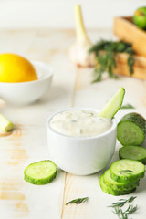 Delicious yogurt sauce with cucumber in bowl on white table