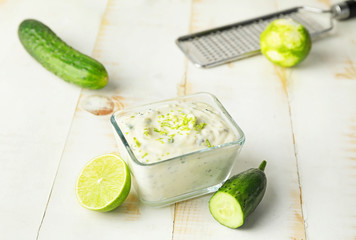 Delicious yogurt sauce with cucumber in bowl on white table