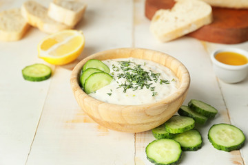 Delicious yogurt sauce with cucumber in bowl on white table