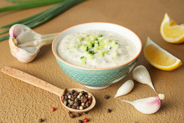 Delicious yogurt sauce with cucumber in bowl on color background