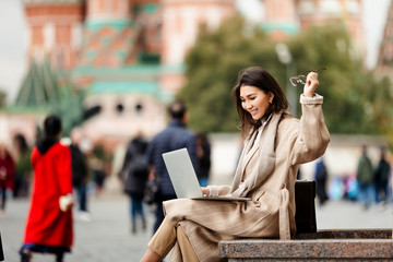 A student from China is sitting with a laptop on red square, and from the successful academic year, throws her hands up