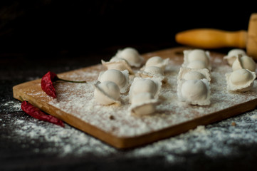 modeling homemade Italian dumplings or ravioli on a dark background with scattered flour, a wooden rolling pin on the table and chili pepper