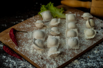 modeling homemade Italian dumplings or ravioli on a dark background with scattered flour, a wooden rolling pin on the table and chili pepper