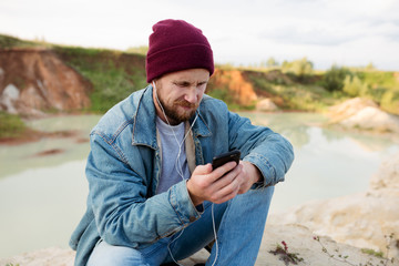 A bearded man sits and communicates in a work chat during a vacation, which is not very happy and his face depicts emotions of discontent