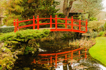 Red bridge over water in a formal garden