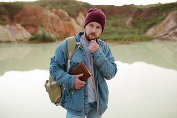 A bearded man, thinking about something, standing in front of a lake with a beautiful bluish-green hue